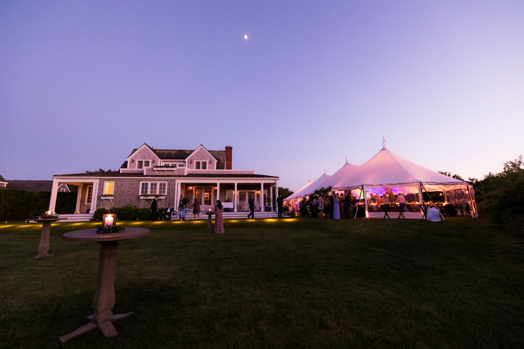 Wedding tent glowing at dusk beside a Nantucket house